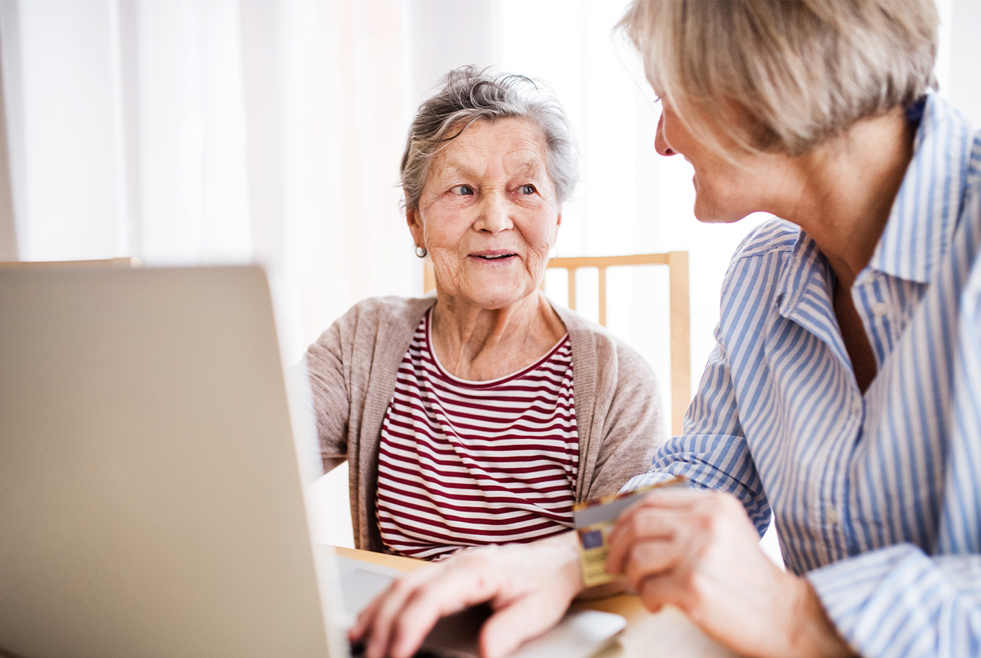 An older woman and a younger woman sitting together, focused on a laptop screen, engaged in a conversation.