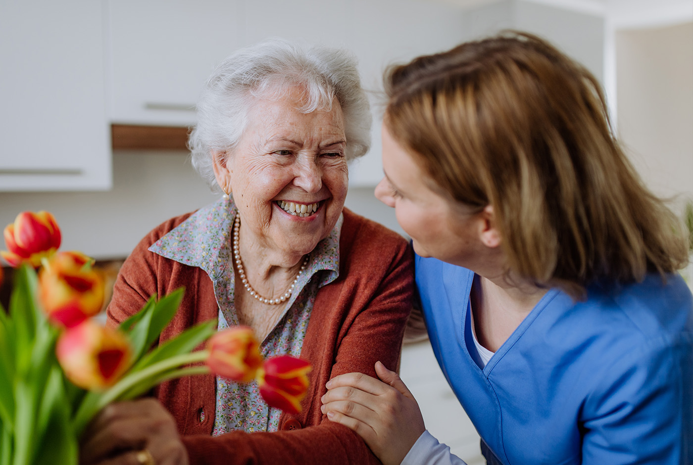 A woman happily holds a bouquet of flowers while smiling at an older woman. A heartwarming moment between generations.