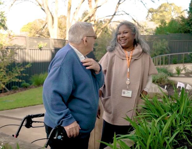 An elderly couple engaged in conversation amidst a serene garden setting.