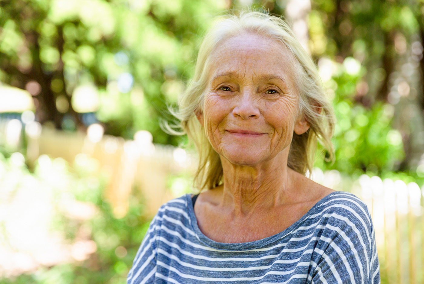 An older woman with a joyful expression, enjoying herself in a park surrounded by nature's beauty.