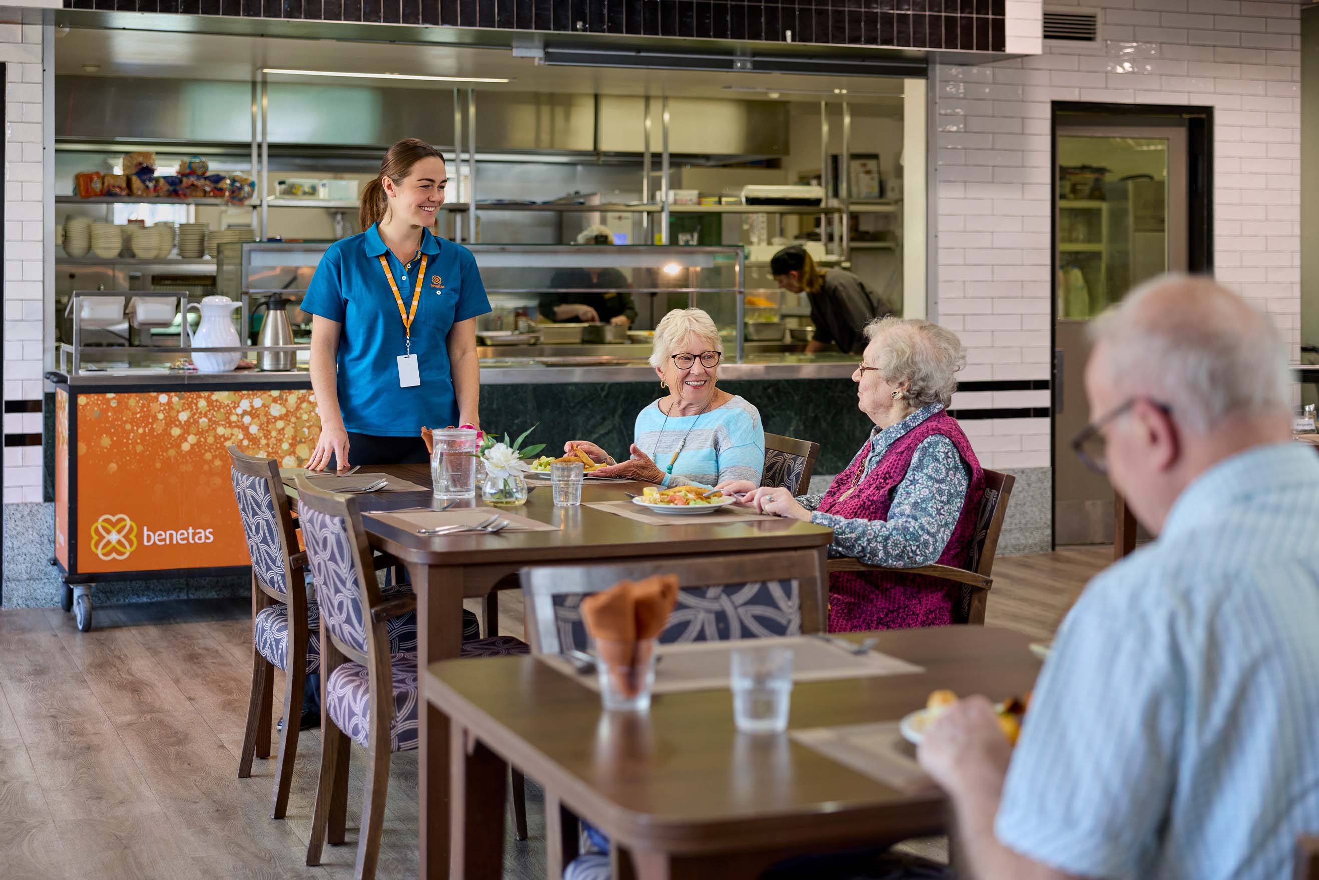 Residents enjoying a meal with support from a Benetas team member in the bistro at Benetas Eaglehawk