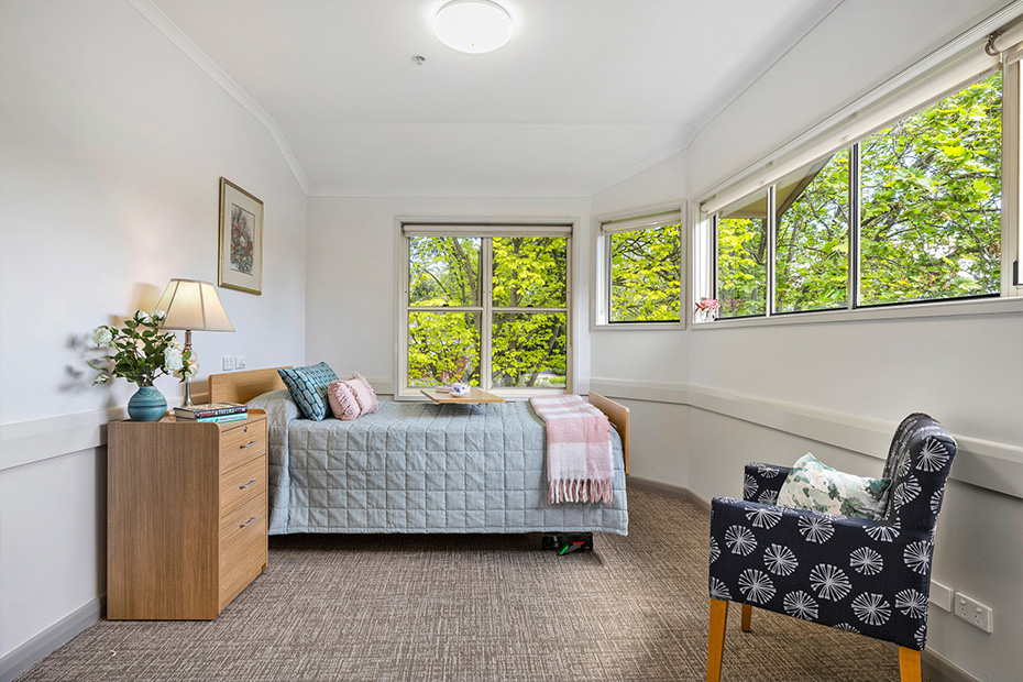 A cozy bedroom with a comfortable bed, a chair, and a window offering a view of the outside world.