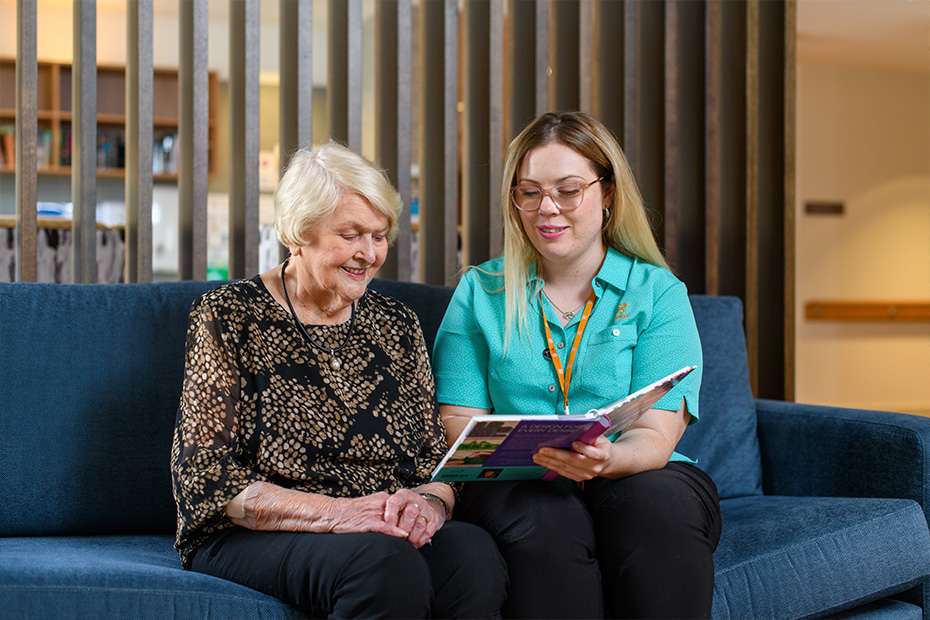 A young woman sitting on a couch with an older Australian woman, engaged in a conversation.
