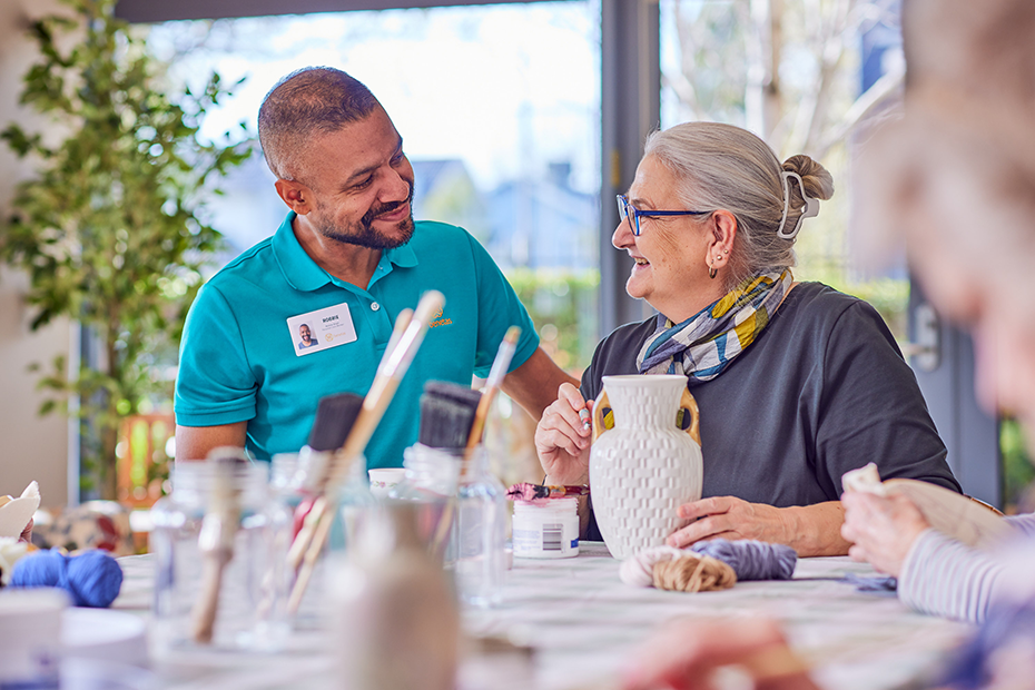 A man and woman engaged in conversation at a crafts table, displaying attentive body language and exchanging ideas.