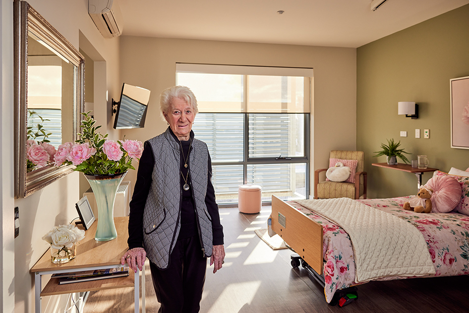 A Colton Close resident woman standing in her room, holding onto a walker for support.