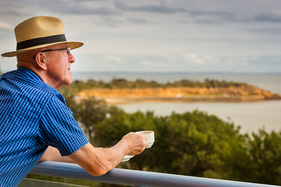 A man in a hat and blue shirt enjoying the ocean view from a balcony.