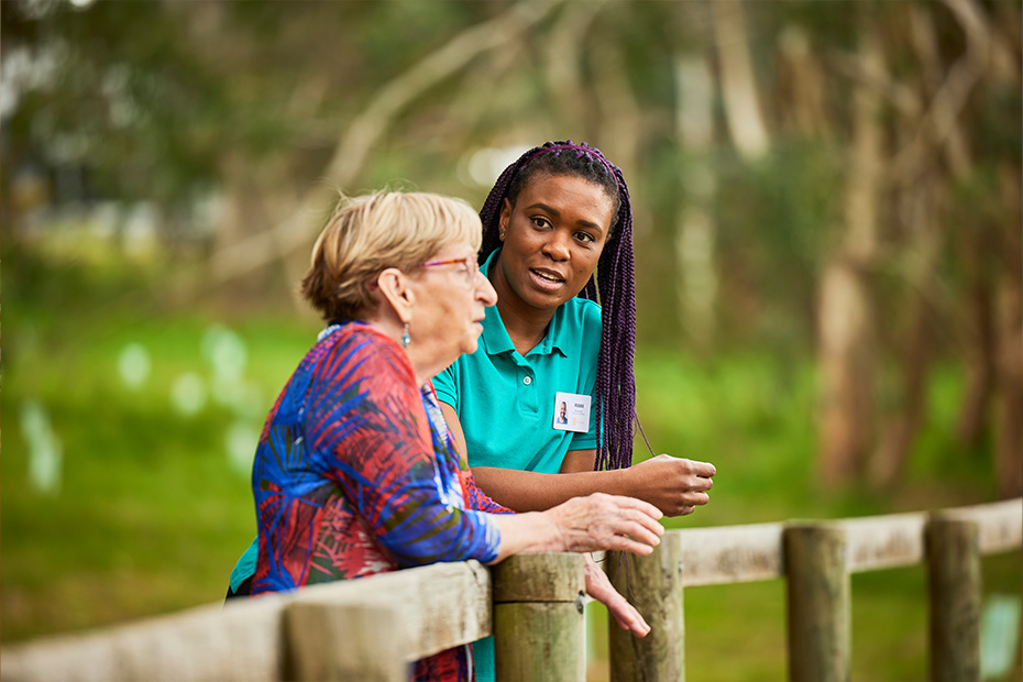 A woman and an older woman standing on a fence, enjoying a conversation and the beautiful view.