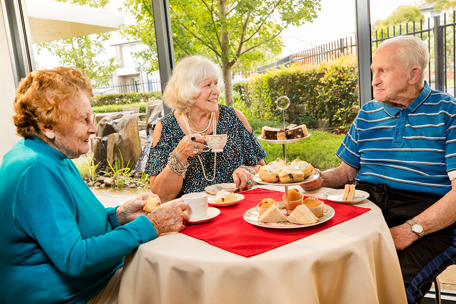 Three residents people enjoying tea and cake together at a table, sharing stories and cherishing their time together.