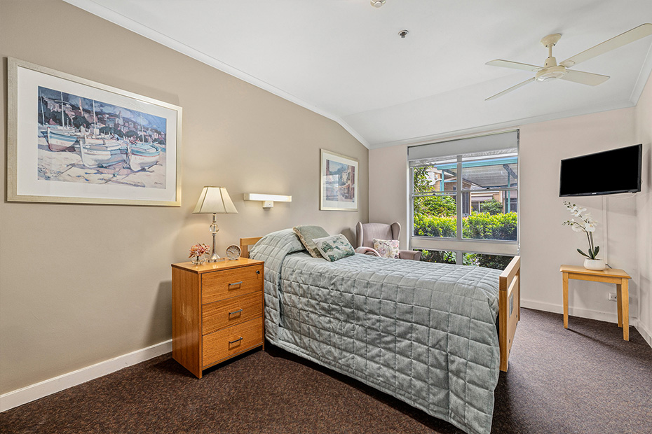 A cozy bedroom with a comfortable bed, a sleek television, and a large window offering natural light.