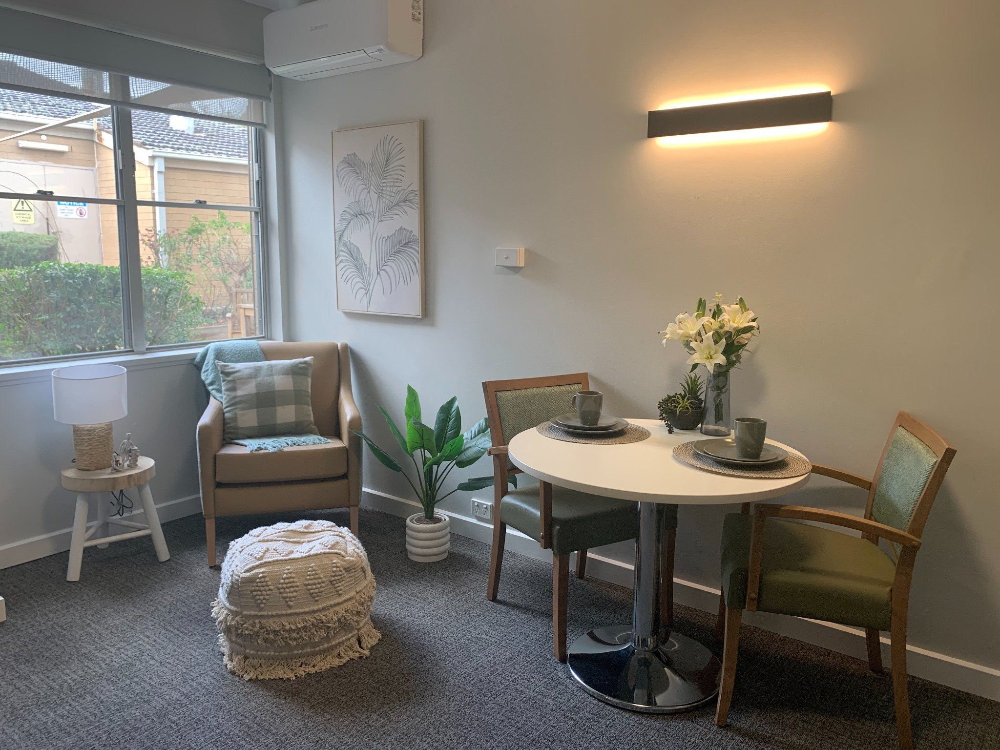 Premium aged care room with dining table set for two, armchair by the window, soft lighting, and modern décor at Benetas.