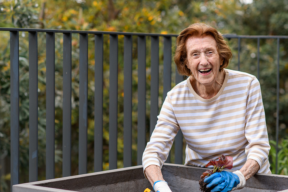 A resident radiates joy as she sits in a serene garden, her face beaming with a warm smile.