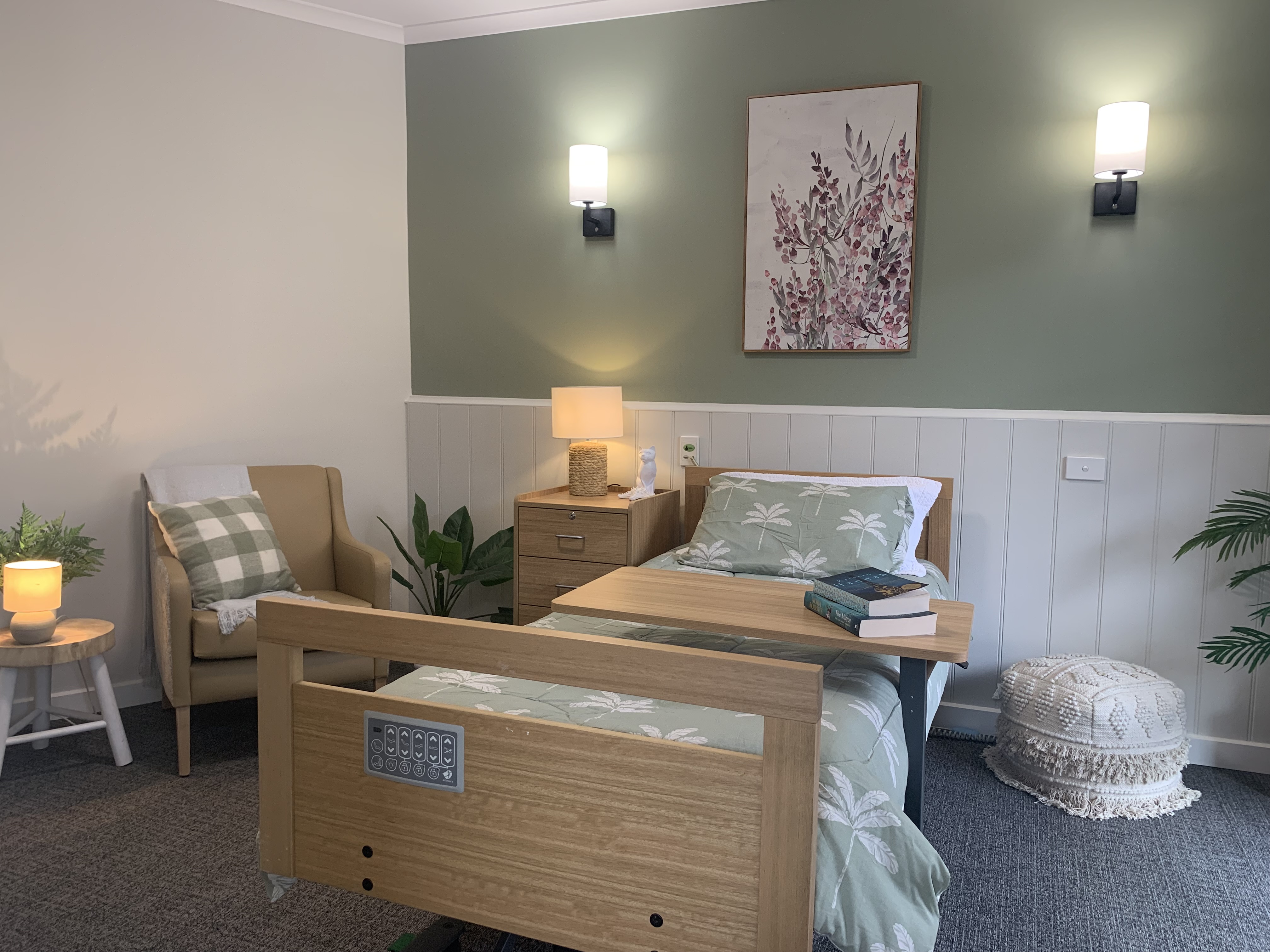 Modern aged care bedroom with a single bed, armchair, bedside table, soft lighting, and calming green decor at Benetas.