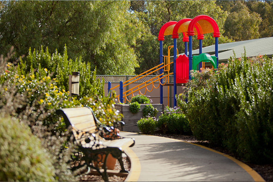 A serene park with a colorful playground and a solitary bench, offering a peaceful spot for relaxation and play.