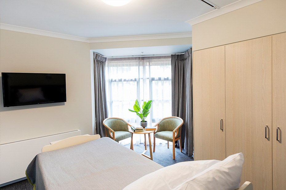 Cozy bedroom with a bed, chair, TV, and window, creating a comfortable and relaxing space.