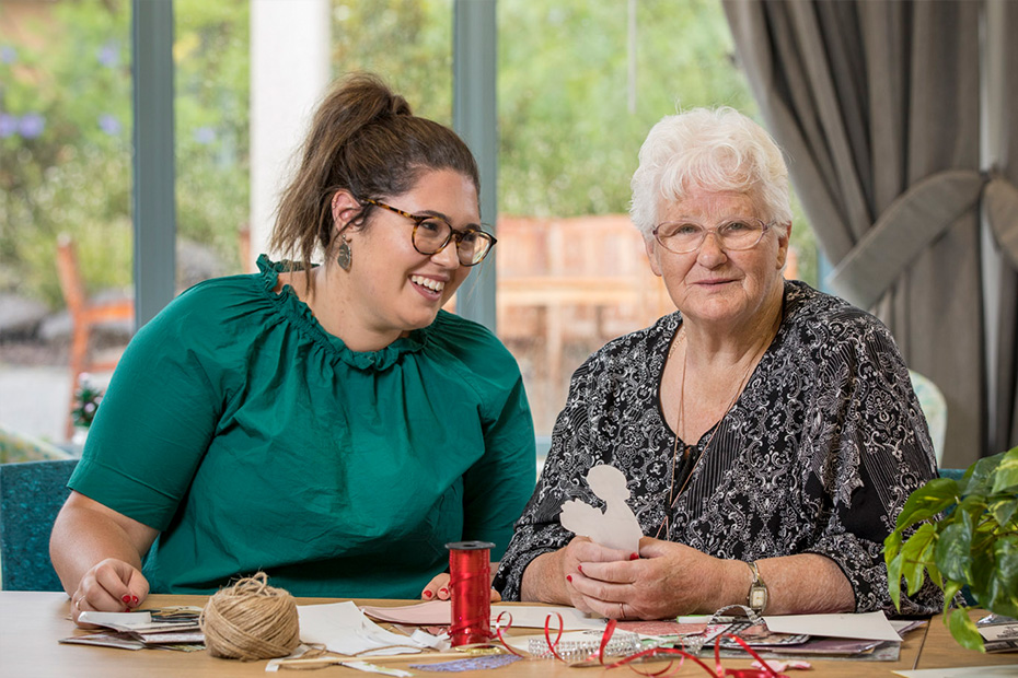 Two women sitting at a table, engrossed in a craft project, showcasing their creativity and collaboration.