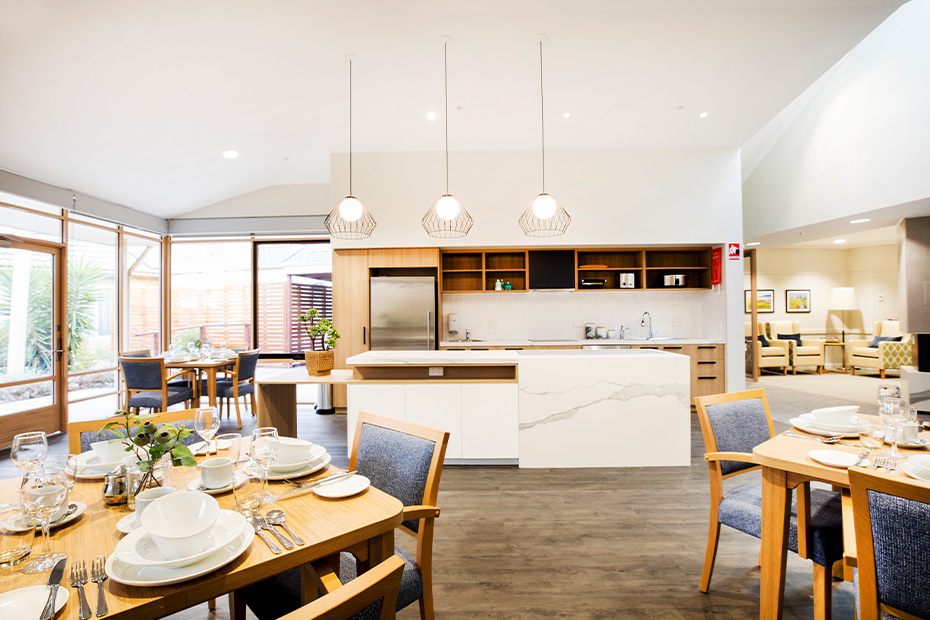 A well-lit dining room with a modern kitchen and a spacious dining table for gatherings.