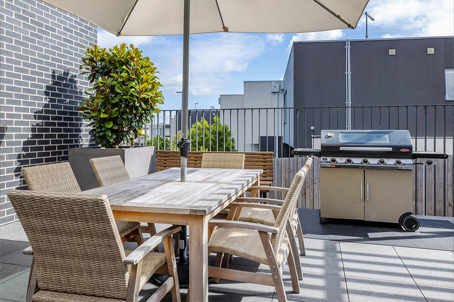 A patio with a table, chairs, and an umbrella providing shade.