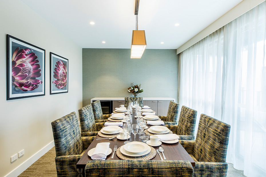 A dining room table with chairs and a large painting hanging on the wall.