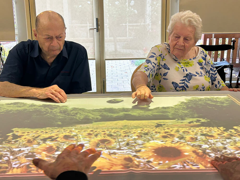 Elderly couple enjoying an interactive game, benefiting from Tovertafel technology at Benetas Clarinda on the Park.
