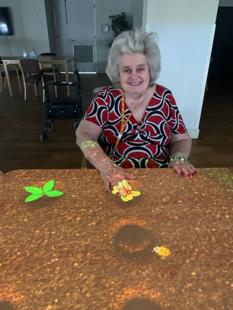 An older woman sitting at a table with a colorful design on its tabletop.