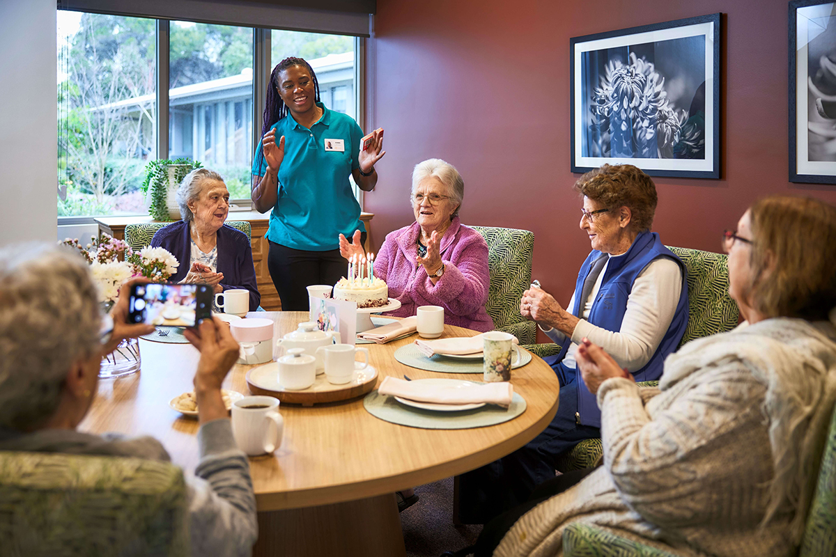 A joyful gathering of seniors at a table, capturing a special moment as a woman snaps a photo.