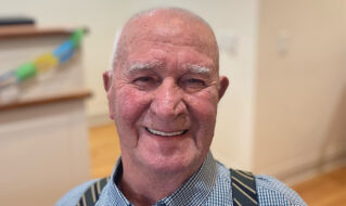 An elderly man wearing suspenders and a cheerful expression on his face.