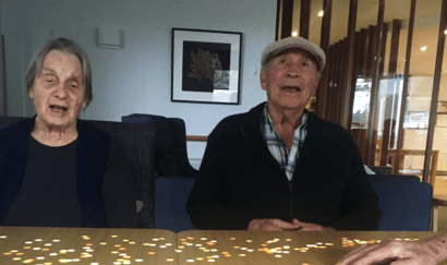 Two older people sitting at a table with a colorful design on the table top.