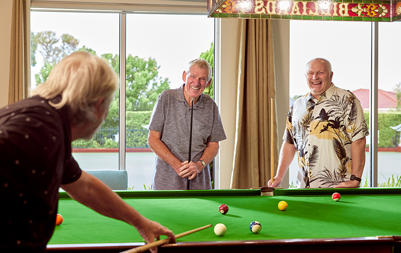 Three older men playing pool in a dimly lit room, focusing on their precise shots and intense concentration.