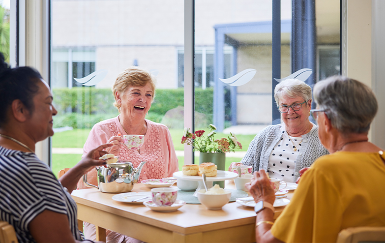 Four women enjoying a conversation over tea and coffee at a table.