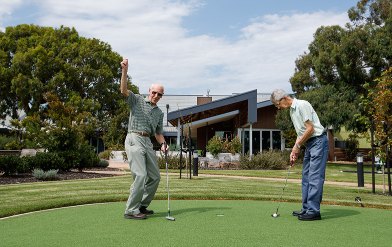 Two men playing golf on a putting green, focusing on their swings and aiming for the hole.