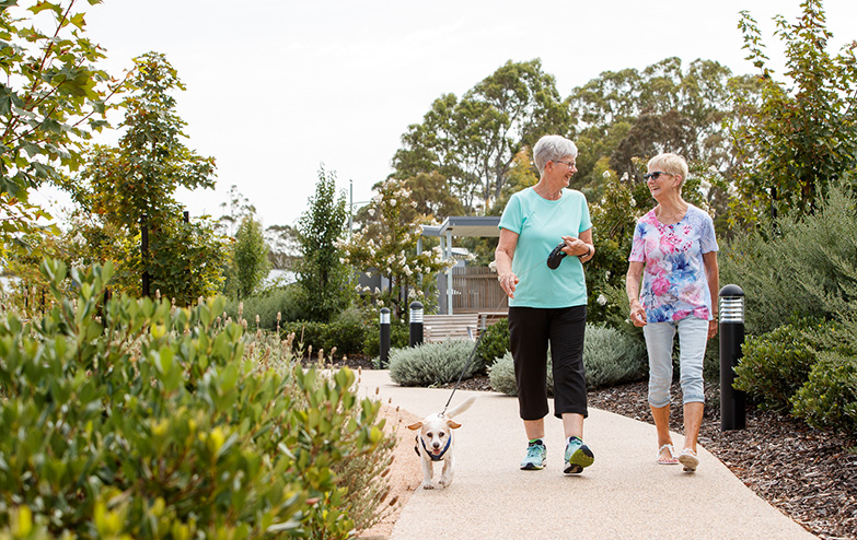 Two women happily walking their dog on a scenic path.