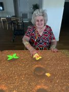 An older woman sitting at a table with a colorful design on its tabletop.