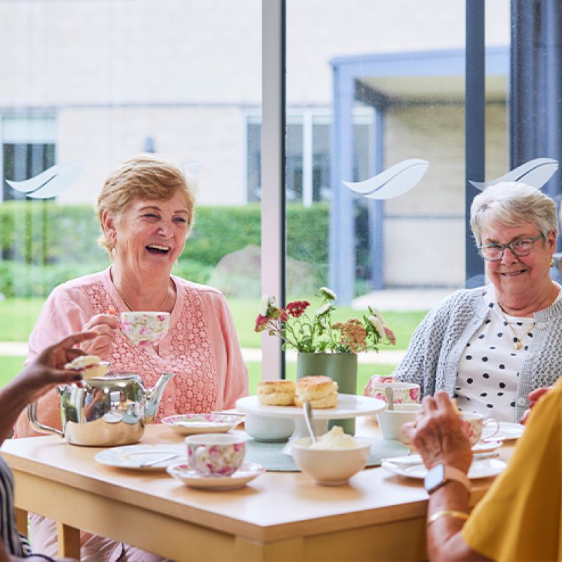 Four women enjoying a conversation over tea and coffee at a table.