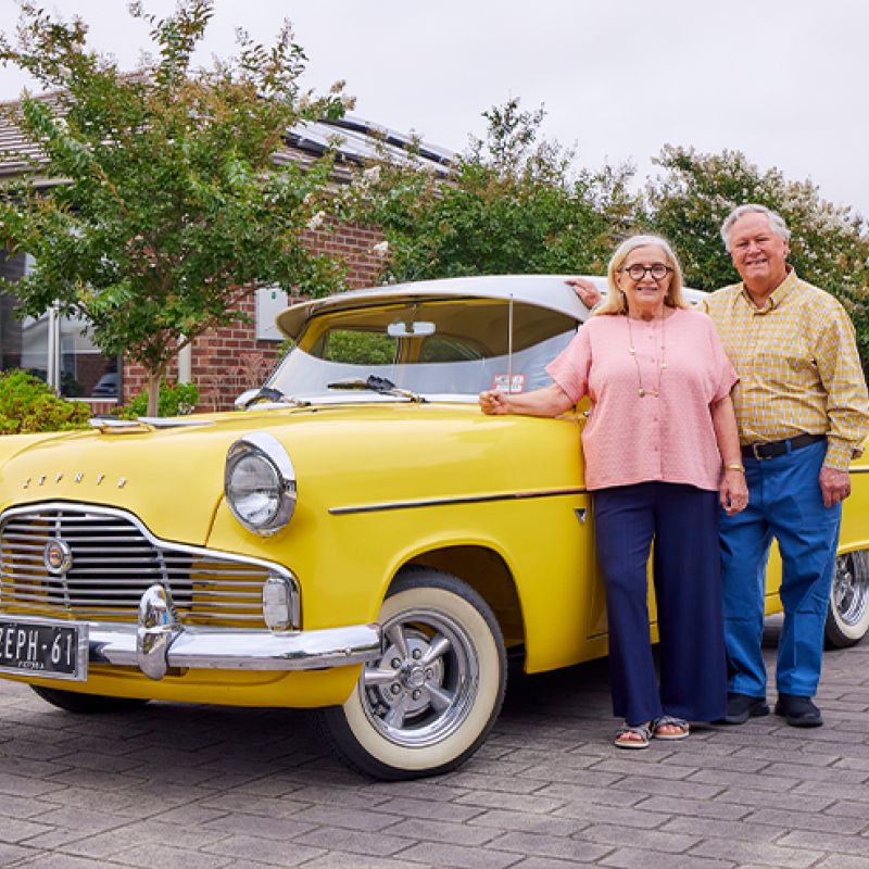 A couple posing beside a vibrant yellow car, exuding a sense of joy and adventure.