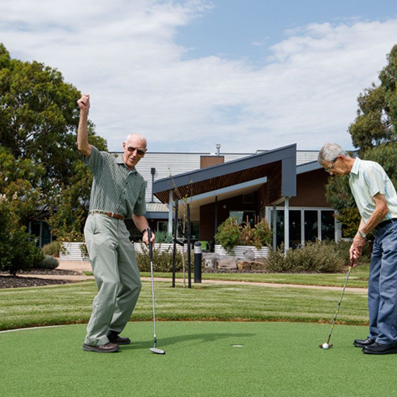 Two men playing golf on a putting green, focusing on their swings and aiming for the hole.
