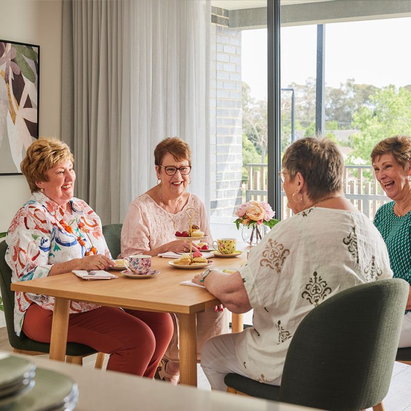  Four women sitting at a table in a room, engaged in conversation and enjoying each other's company.