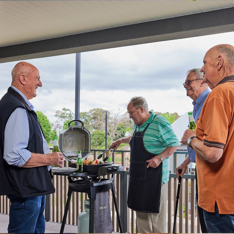 Three men grilling on a balcony.